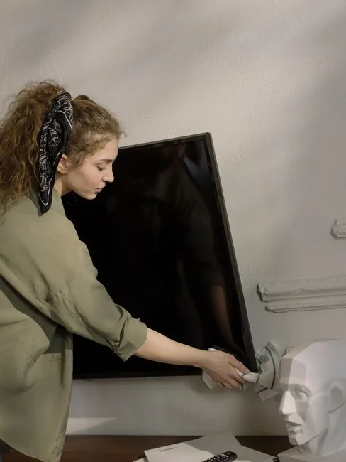 A woman carefully wraps a sofa in protective material while packing boxes in a bright room.